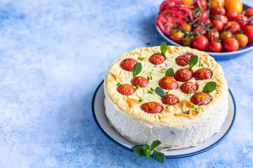 Savoury cheesecake with tomatoes decorated with mint, blue concrete background.