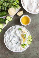 Traditional greek tzatziki dip sauce with grated cucumber, greek yogurt, olive oil and mint, green concrete background. Top view.