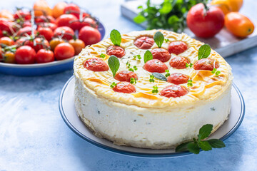 Savoury cheesecake with tomatoes decorated with mint, blue concrete background.