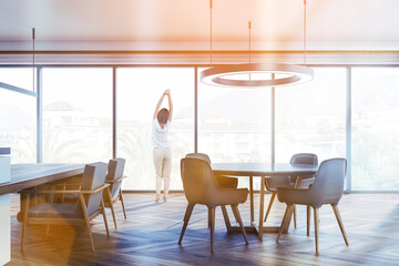 Woman in living room interior with round table and panoramic window, toned image