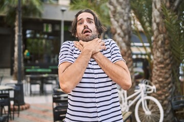 Young hispanic man with beard outdoors at the city shouting and suffocate because painful strangle. health problem. asphyxiate and suicide concept.