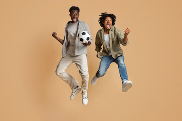 Goal. Two Overjoyed Black Male Friends Jumping In Air With Football Ball