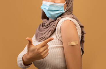 I got my covid-19 vaccine. Vaccinated muslim lady showing arm after vaccination and pointing at plaster, closeup, crop