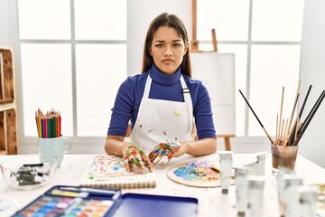 Young brunette woman at art studio with painted hands skeptic and nervous, frowning upset because...