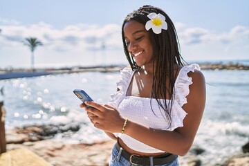 Young african american girl smiling happy using smartphone at the beach
