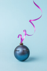 Naklejka na ściany i meble A dark blue ball with eyelashes and a bright ribbon on a blue background. The minimum concept of the New Year.