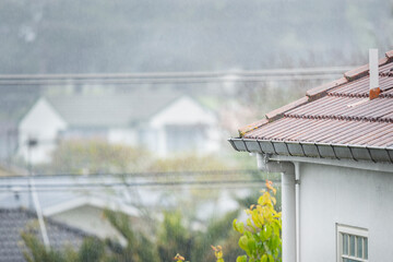 Roof gutter overflow in the rain. Visible raindrops against out-of-focus houses in the background.