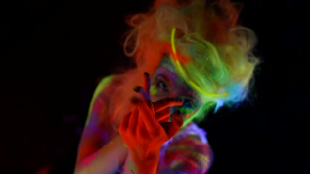 portrait of a woman with multicolored neon hair and skin on a dark background. she moves hands beautifully. top view