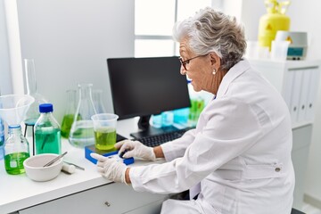 Senior grey-haired woman wearing scientist uniform weighing liquid at laboratory