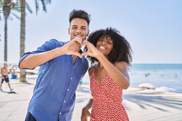 Young interracial couple outdoors on a sunny day smiling in love doing heart symbol shape with hands. romantic concept.