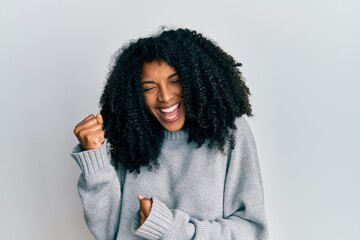 African american woman with afro hair wearing casual winter sweater celebrating surprised and amazed for success with arms raised and eyes closed