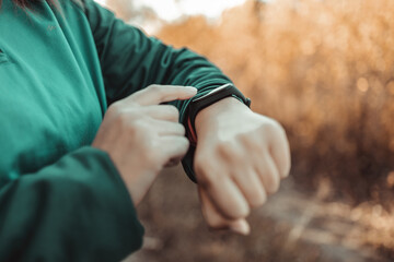 Athletic female using fitness tracker or smart watch between run training outdoors, checking heart rate