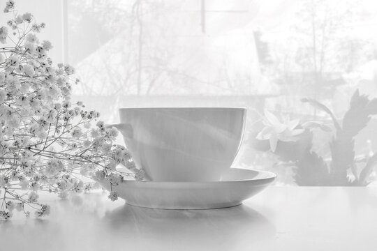 High key photograph of a porcelain white mug with a saucer and white gypsophila. The concept of romance, breakfast