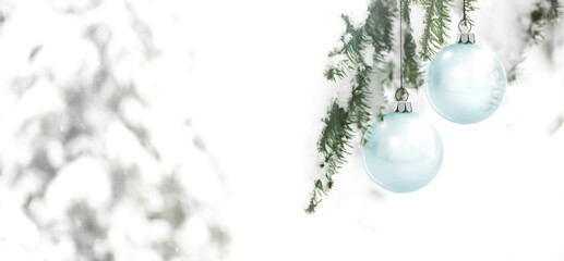Gläserne Weihnachtskugeln an einem Tannenzweig vor einem verschneiten unscharfen Hintergrund