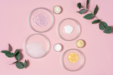Cosmetic products, scrub, face serum and gel in many petri dishes on a pink background. Cosmetics laboratory research concept.