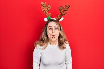 Middle age caucasian woman wearing cute christmas reindeer horns afraid and shocked with surprise...