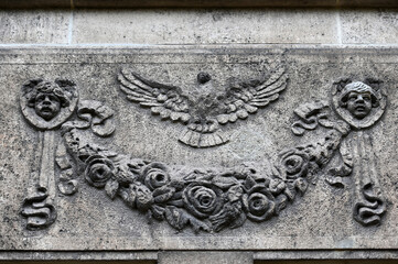 An old, weathered sandstone relief of a headless bird with spread wings in front of an old crypt in Berlin-Germany.