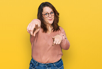 Young plus size woman wearing casual clothes and glasses pointing to you and the camera with...