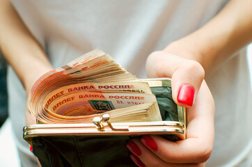 A girl holds a purse with Russian money in her hands, close-up. Concept A lot of money, prosperity.