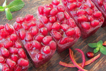 fresh frozen pomegranate seeds in ice cubes, arranged in a row, in a wooden plate and decorated...