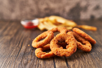  Bunch of breaded onion rings and potato chips on a wooden surface