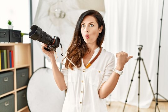 Beautiful caucasian woman working as photographer at photography studio surprised pointing with hand finger to the side, open mouth amazed expression.