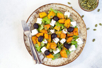 Healthy salad with fried pumpkin, feta cheese, olives, salad greens, pumpkin seeds on the light grey background. Macro.