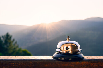 Silver vintage bell on village reception desk in the morning sunrise mountain. Eco, camping hotel service, registration. - obrazy, fototapety, plakaty