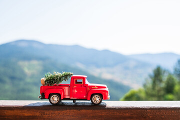 Red retro small car carrying christmas tree in the mountain. Winter holiday concept