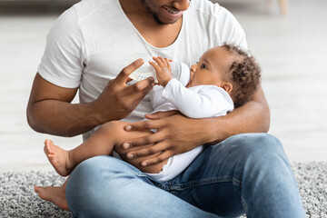 Adorable Black Baby Drinking Water Form Bottle While Lying On Fathers Lap