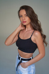 Obraz premium Elegant woman with natural make-up and wavy hair. Pretty girl in black top and white blue jeans with black belt posing against blue background in studio