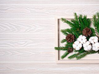 Fototapeta na wymiar White tray with Christmas tree fir branches, cotton and cones on wooden background, top view. Holiday sustainable eco diy decor and new year preparation flatlay. Rustic winter concept with copy space