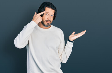 Middle age caucasian man wearing casual clothes confused and annoyed with open palm showing copy space and pointing finger to forehead. think about it.