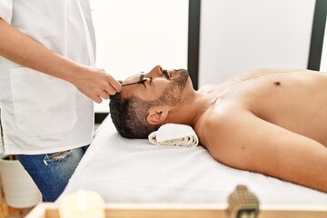 Fototapeta na wymiar Young hispanic man having eyebrows treatment at beauty center