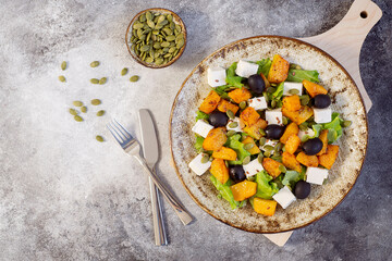 Healthy salad with fried pumpkin, feta cheese, olives, salad greens, pumpkin seeds, olive oil on the dark grey background. Horizontal view. Top view.