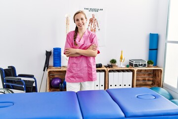 Young caucasian woman wearing physiotherapist uniform standing with arms crossed gesture at physiotherapy clinic