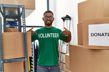 Young arab man pointing with fingers to volunteer uniform at charity center