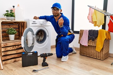 Young indian technician working on washing machine doing money gesture with hands, asking for...