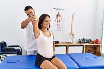 Latin man and woman wearing physiotherapist uniform having pregnancy rehab session at physiotherapy...