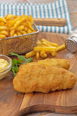 Poisson et frites, sel, sauce et persil sur une planche de bois 