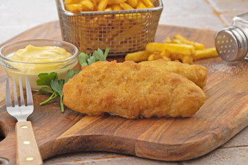 Poisson et frites, sel, sauce et persil sur une planche de bois 