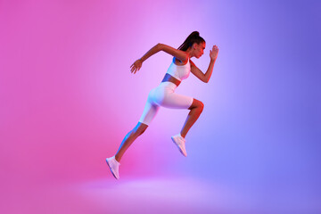 Determined Sporty Woman Running In Mid-Air Over Neon Background, Side-View