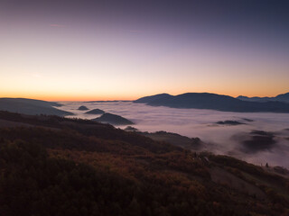 Italy November 2021: aerial view of mountains with fog below in autumn season at sunset