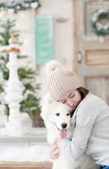 girl hugging a white fluffy samoed dog near front door of a house decorated for christmas
