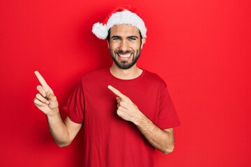 Young hispanic man wearing christmas hat smiling and looking at the camera pointing with two hands...