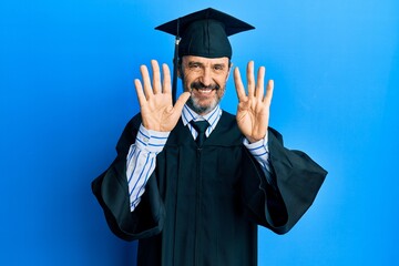 Middle age hispanic man wearing graduation cap and ceremony robe showing and pointing up with fingers number nine while smiling confident and happy.