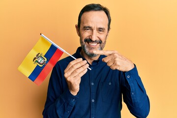 Middle age hispanic man holding ecuador flag smiling happy pointing with hand and finger