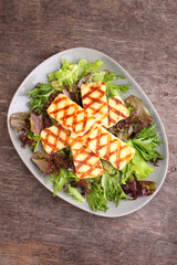 Green salad with fried halloumi cheese in a plate on a old wooden background, top view.