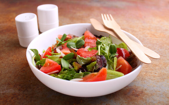 Healthy salad in a white plate of greens, tomatos and microgreen on a old background.
