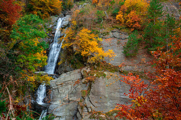 A waterfall flowing from a height through yellowed trees in autumn